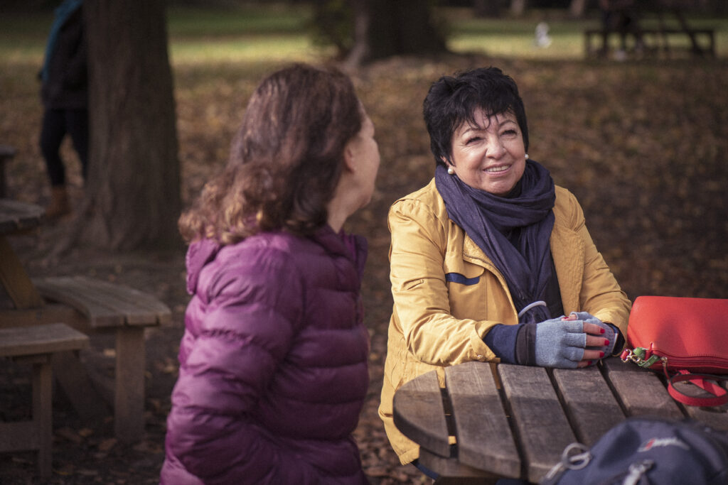 Two women have a conversation, sat in the park