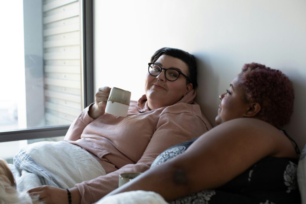 A photo of a female plus-sized couple sat side by side, drinking coffee and smiling