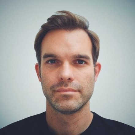 A photo of ben wearing a dark t-shirt in front of a white wall